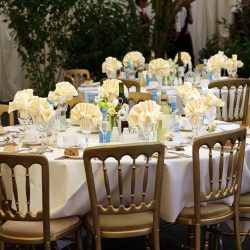 Elegancko nakryte okrągłe stoły weselne z białymi obrusami i kwiatowymi dekoracjami w sali restauracyjnej.