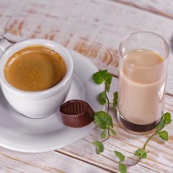 Kawa w filiżance na spodku, obok pralinka i mleko w szklance