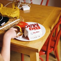 Dziewczyna sięgająca po frytki, które leżą obok pudełka Big Mac